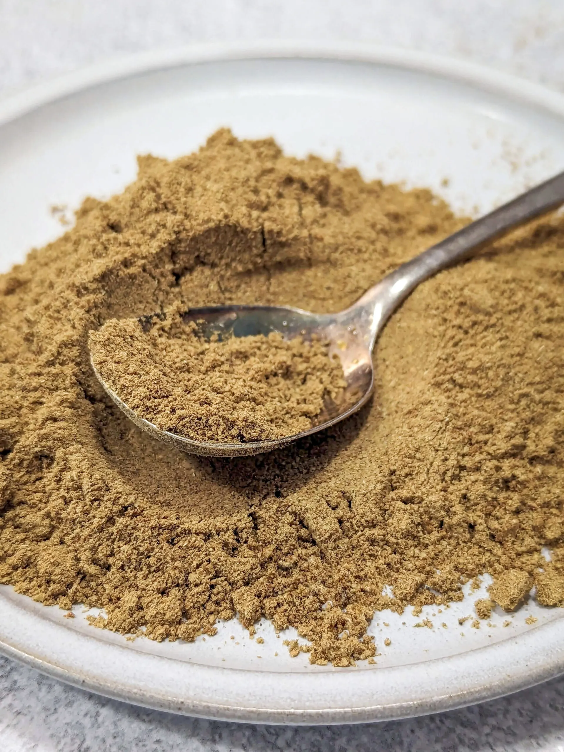 A spoon of Chinese 5 spice over a plate of the spice mixture.