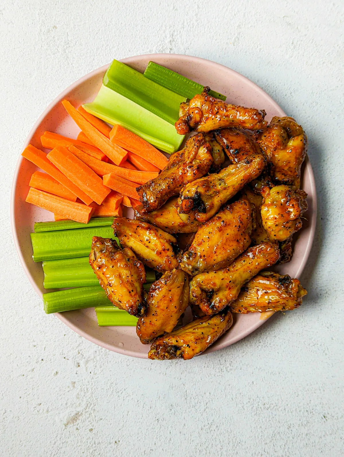 A close up of hot honey lemon pepper wings on a plate with vegetables.