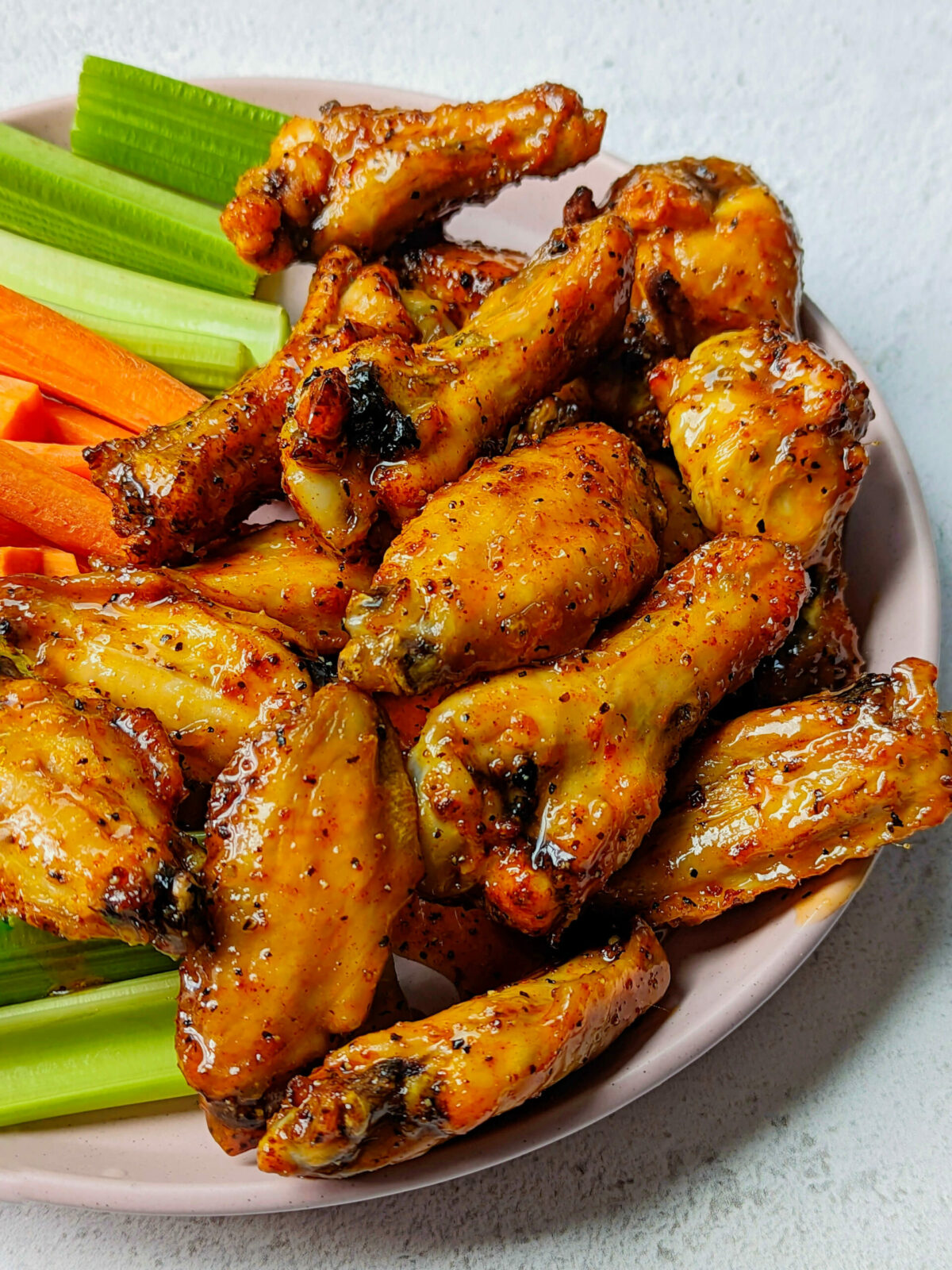 A close up of hot honey lemon pepper wings on a plate with vegetables.