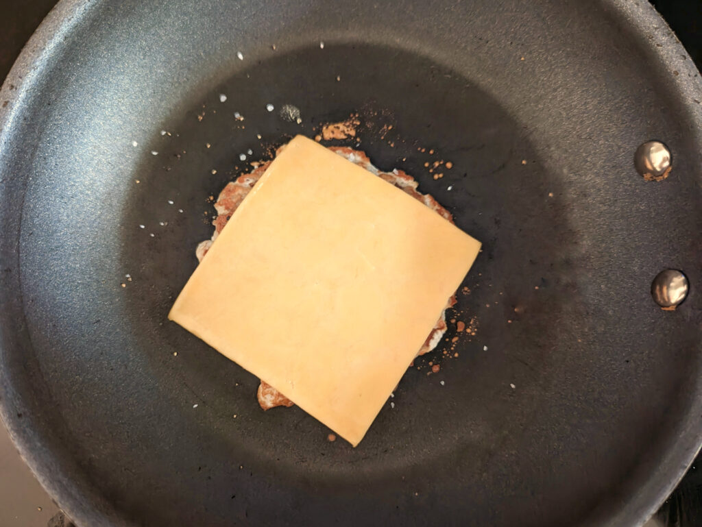 Cheese added to the turkey smash burger on the pan.