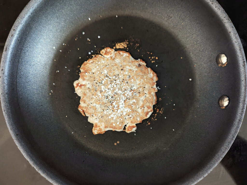 A flipped turkey smash burger sprinkled with salt and pepper.