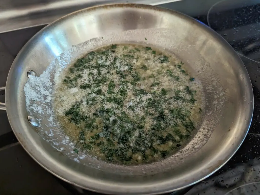 Butter cooking in a skillet with parsley and garlic added.