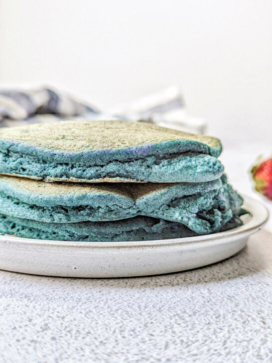 A close up of blue pancakes with strawberries in the background.