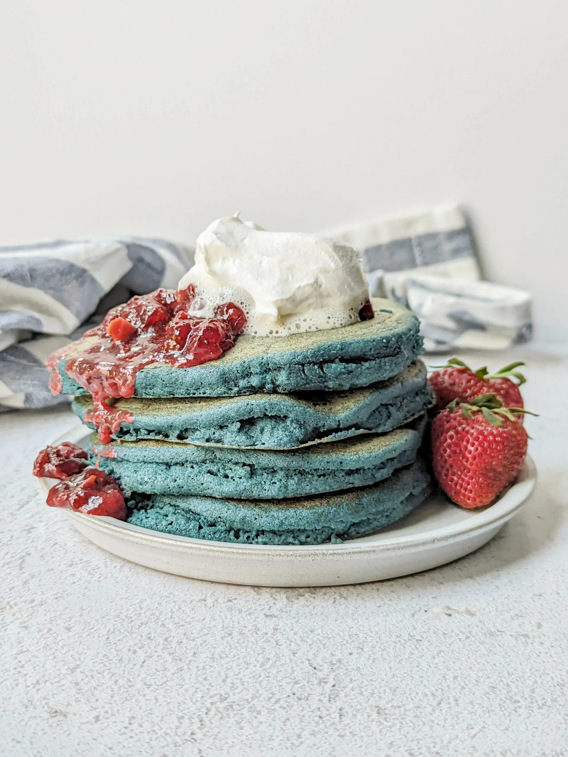 Blue pancakes topped with strawberry compote and whipped cream.