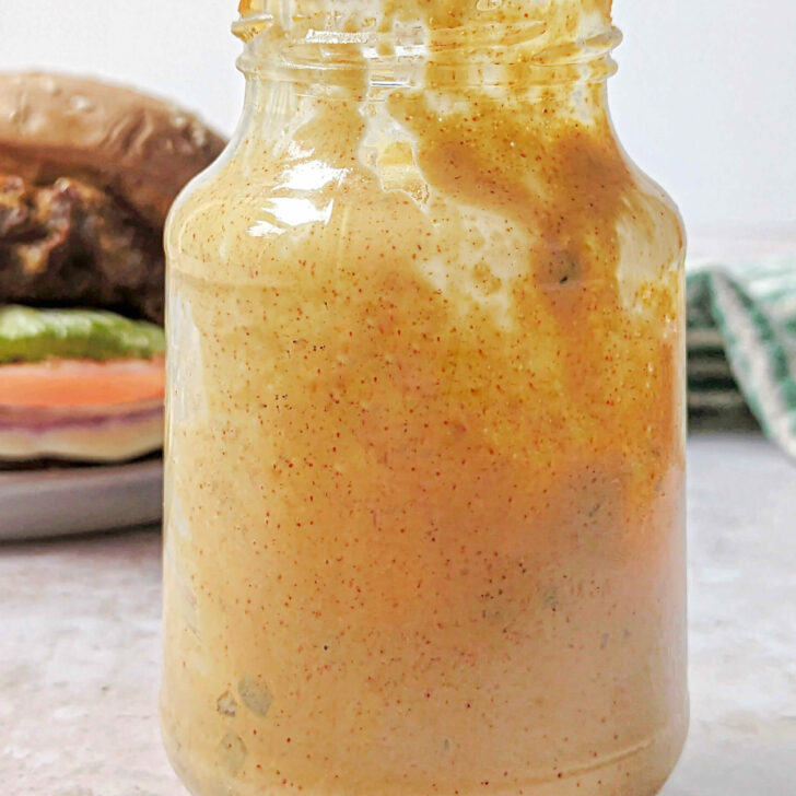 A glass jar filled with our McDonald's Big Mac Sauce Recipe with a burger in the background.