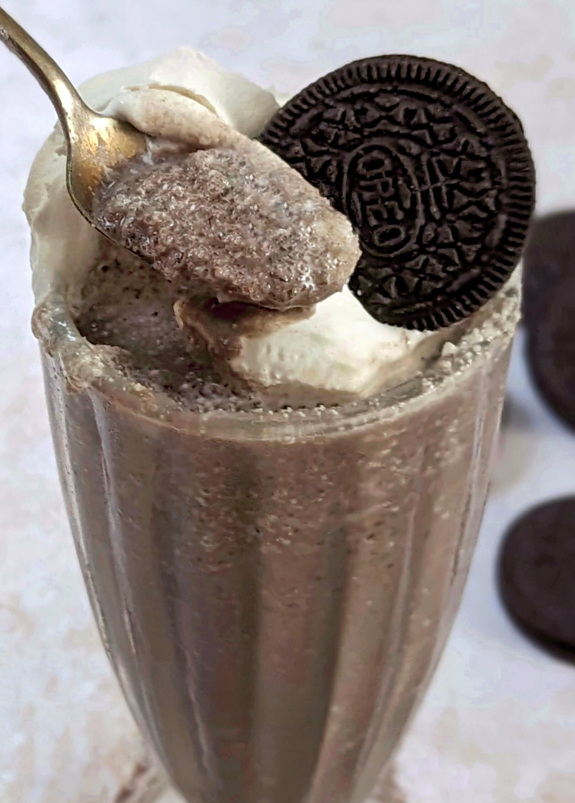 A close up of a milkshake without ice cream with whopped cream and an oreo on top.