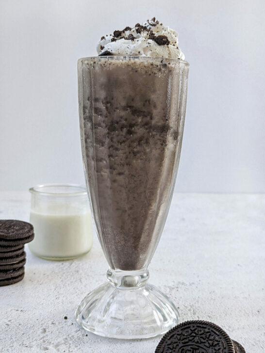 A close up of a milkshake without ice cream with whopped cream and an oreo on top with oreos in the background.