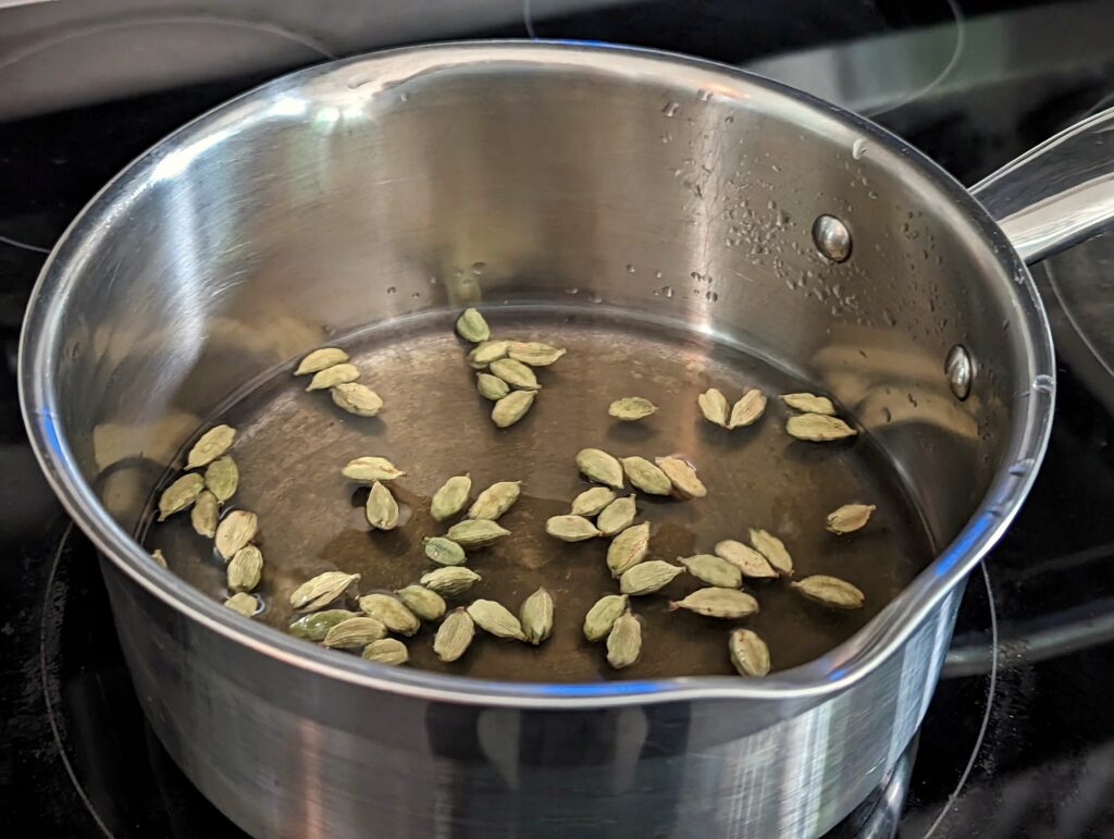 Cardamom pods, water, and honey in a saucepan.