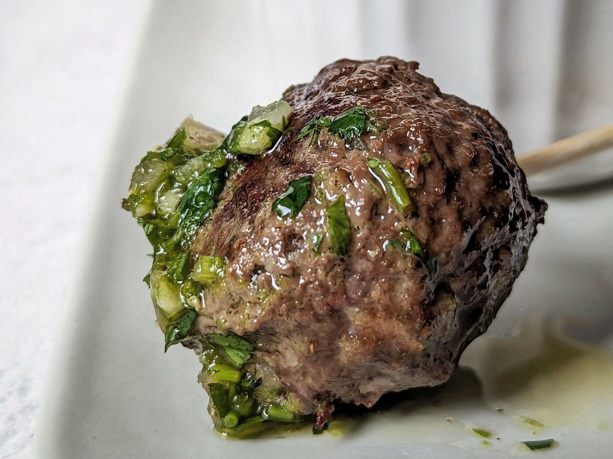 A close up of a meatball dipped in chimichuri.