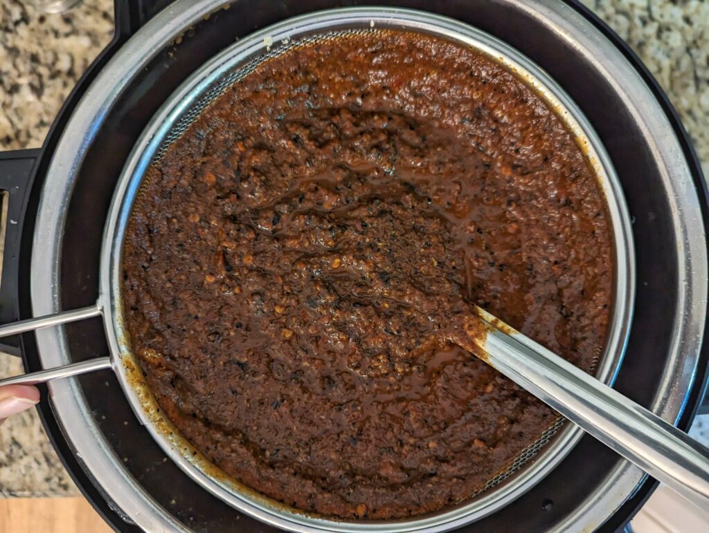 Chili mixture straining through a mesh strainer.