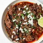 A bowl of birria con consome garnished with onion and cilantro.