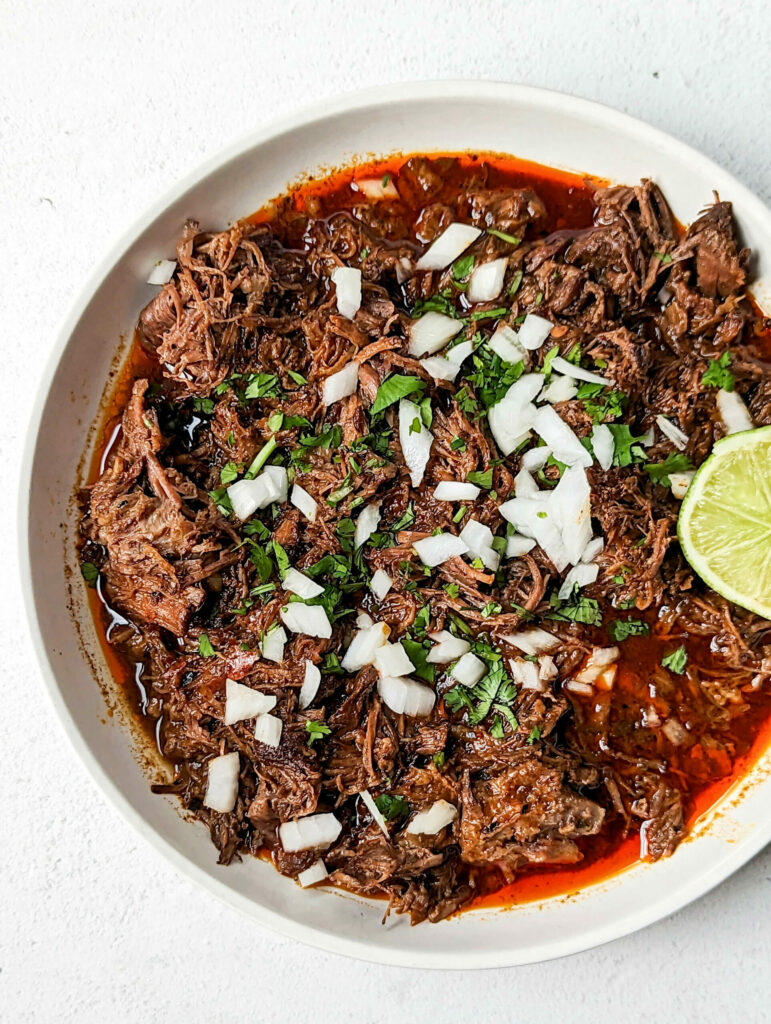 A bowl of birria con consome garnished with onion and cilantro.