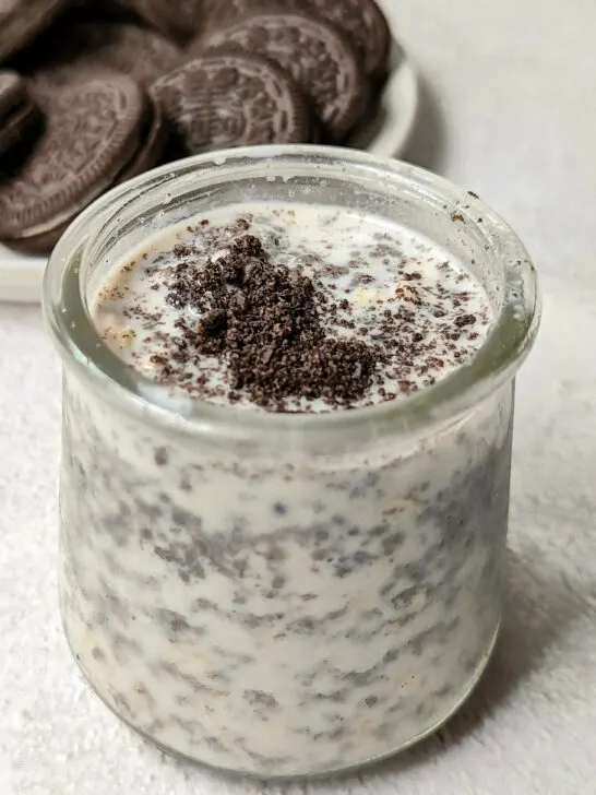 A close up of a small container of oreo overnight oats with oreos in the background.