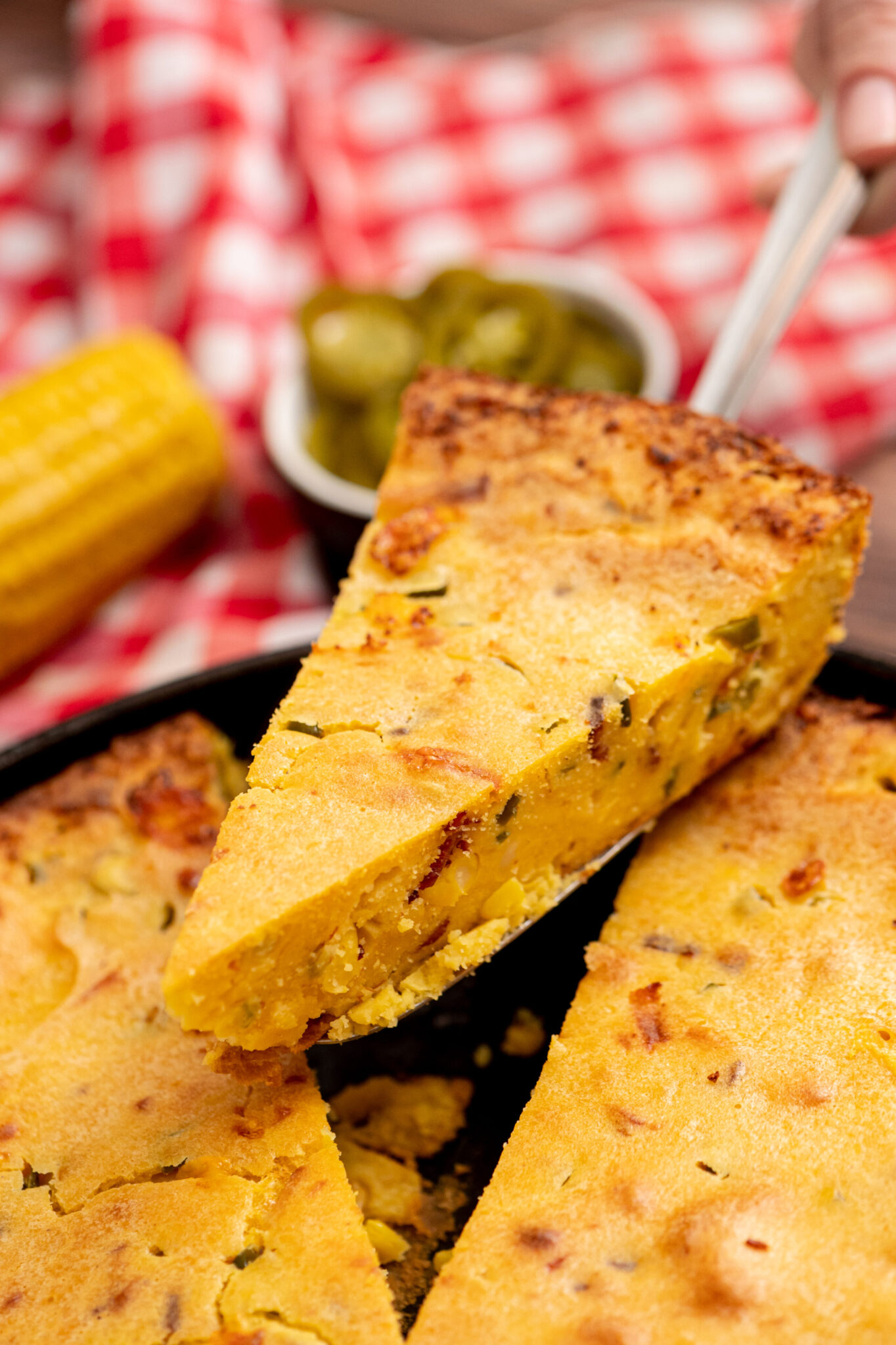 Slices of loaded cornbread on a plate with BBQ sides in the background.