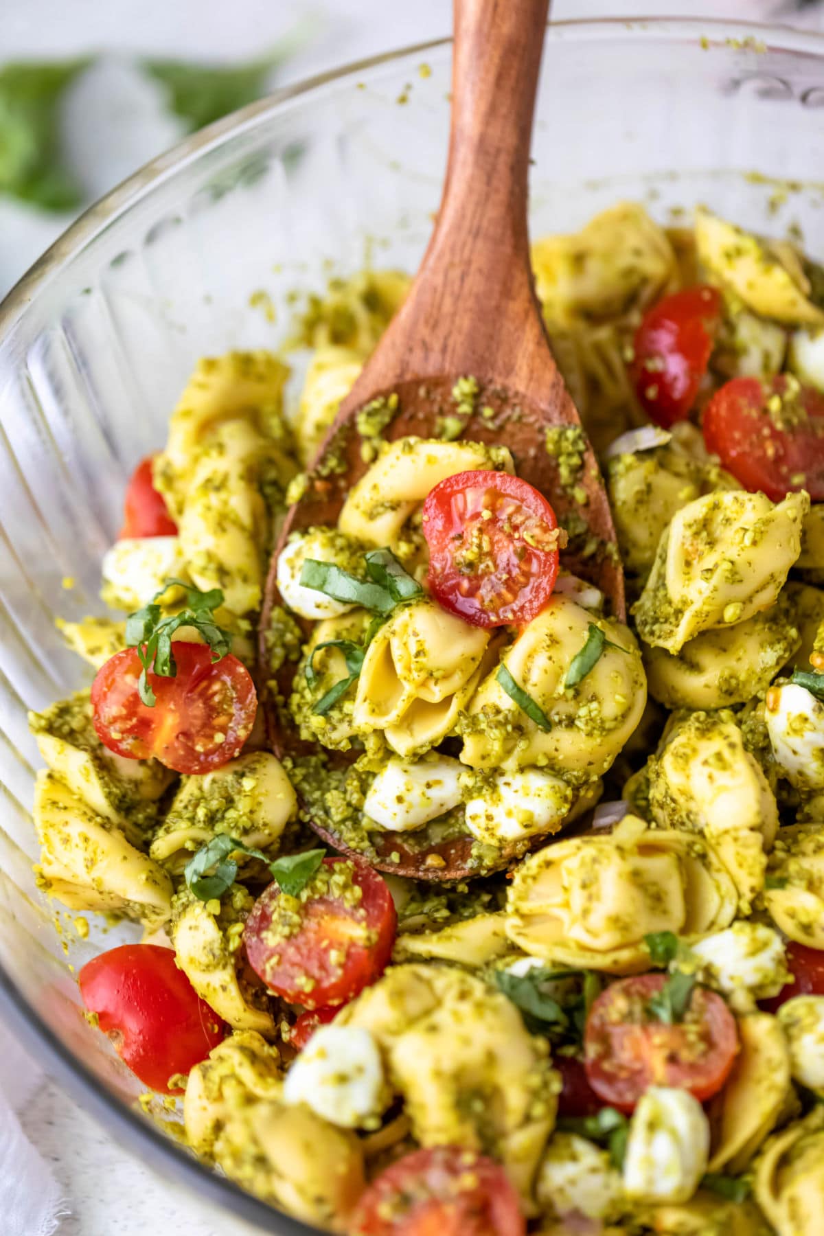 A serving bowl of Pesto tortellini salad with a large spoon in it.