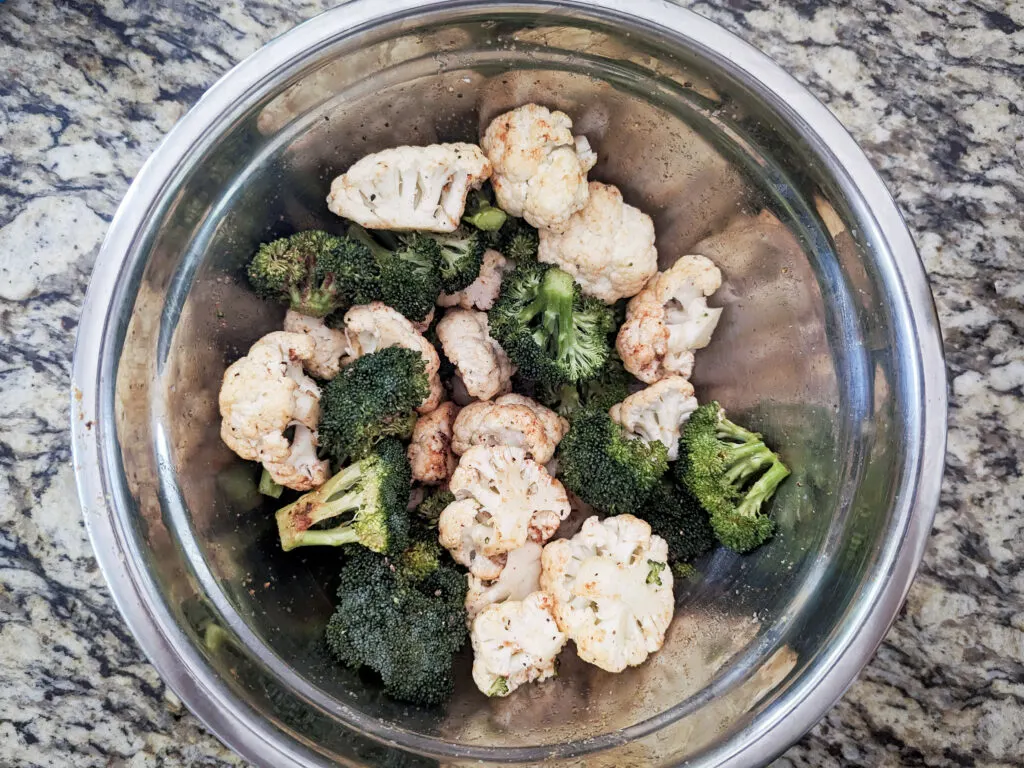 Broccoli and cauliflower tossed in a bowl with spices and olive oil.