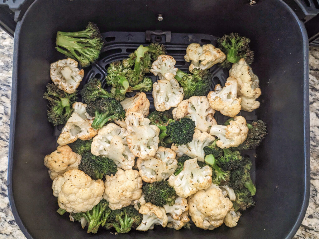 Broccoli and cauliflower in the air fryer basket ready to be shaken.