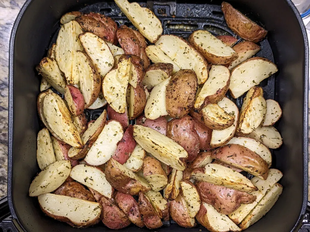 Red potatoes begin shaken in an air fryer basket.