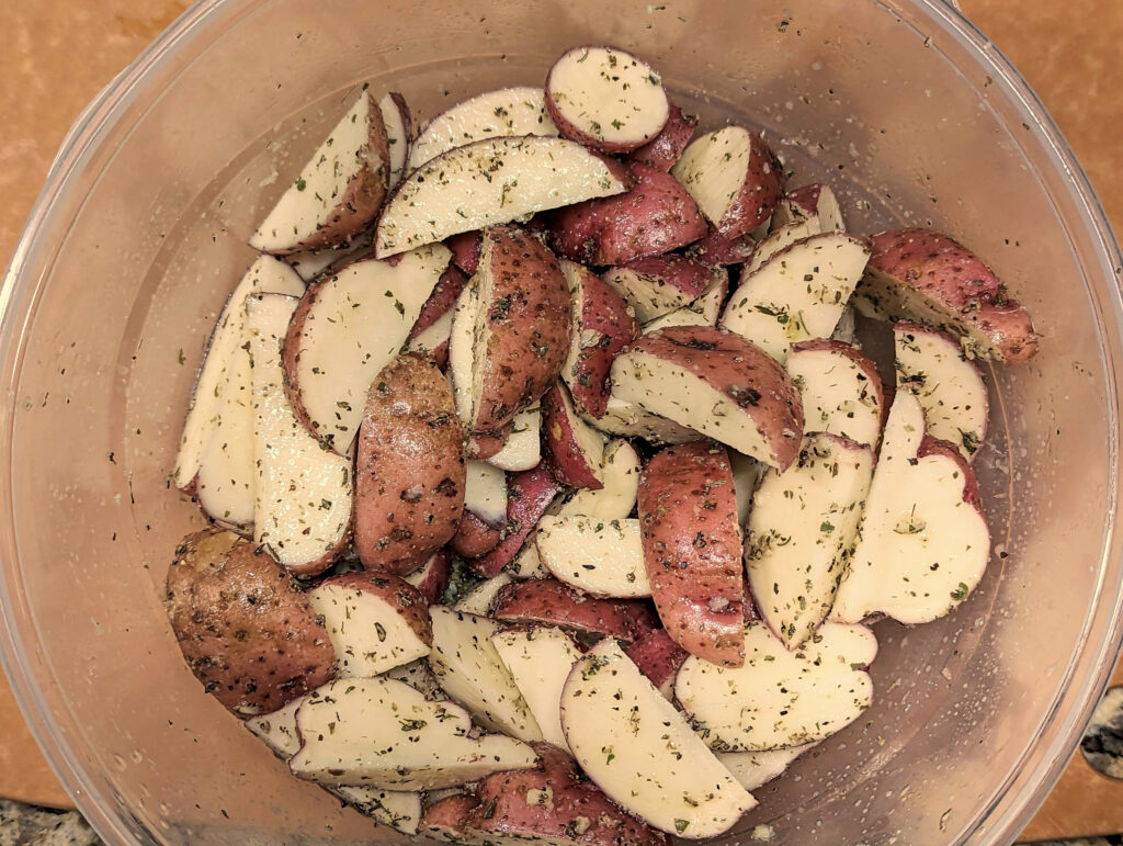 Red potatoes in a marinating bowl with lemon and Greek seasoning.
