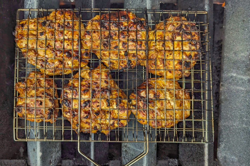 Chicken in a grill basket cooking over flavor bars.