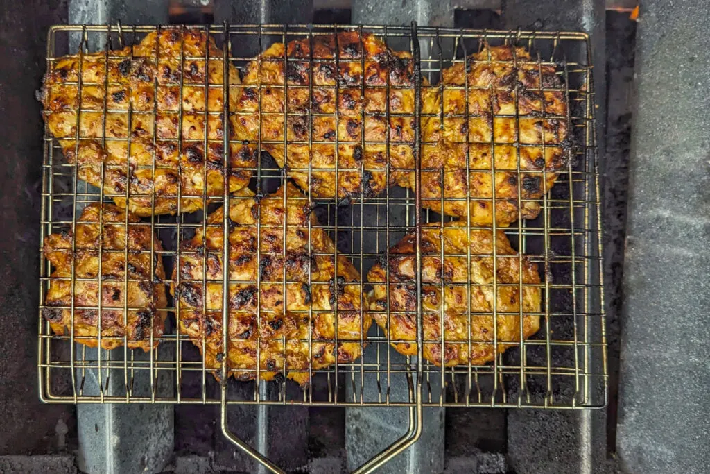 Chicken in a grill basket cooking over flavor bars.
