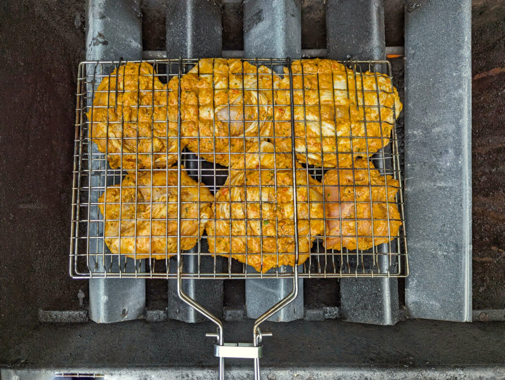 Chicken in a grilling basket cooking over the flavor bars.