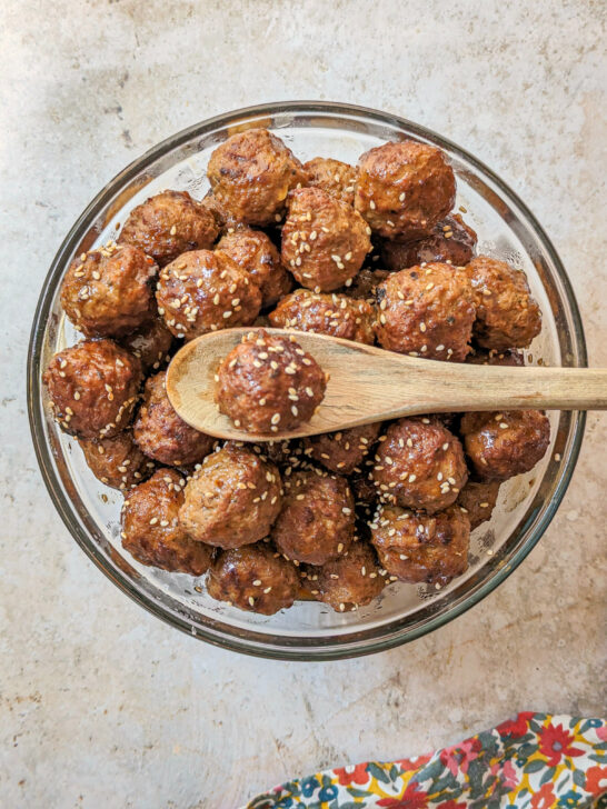 A bowl of Instant Pot Frozen Meatballs with a wooden spoon holding one of the meatballs.