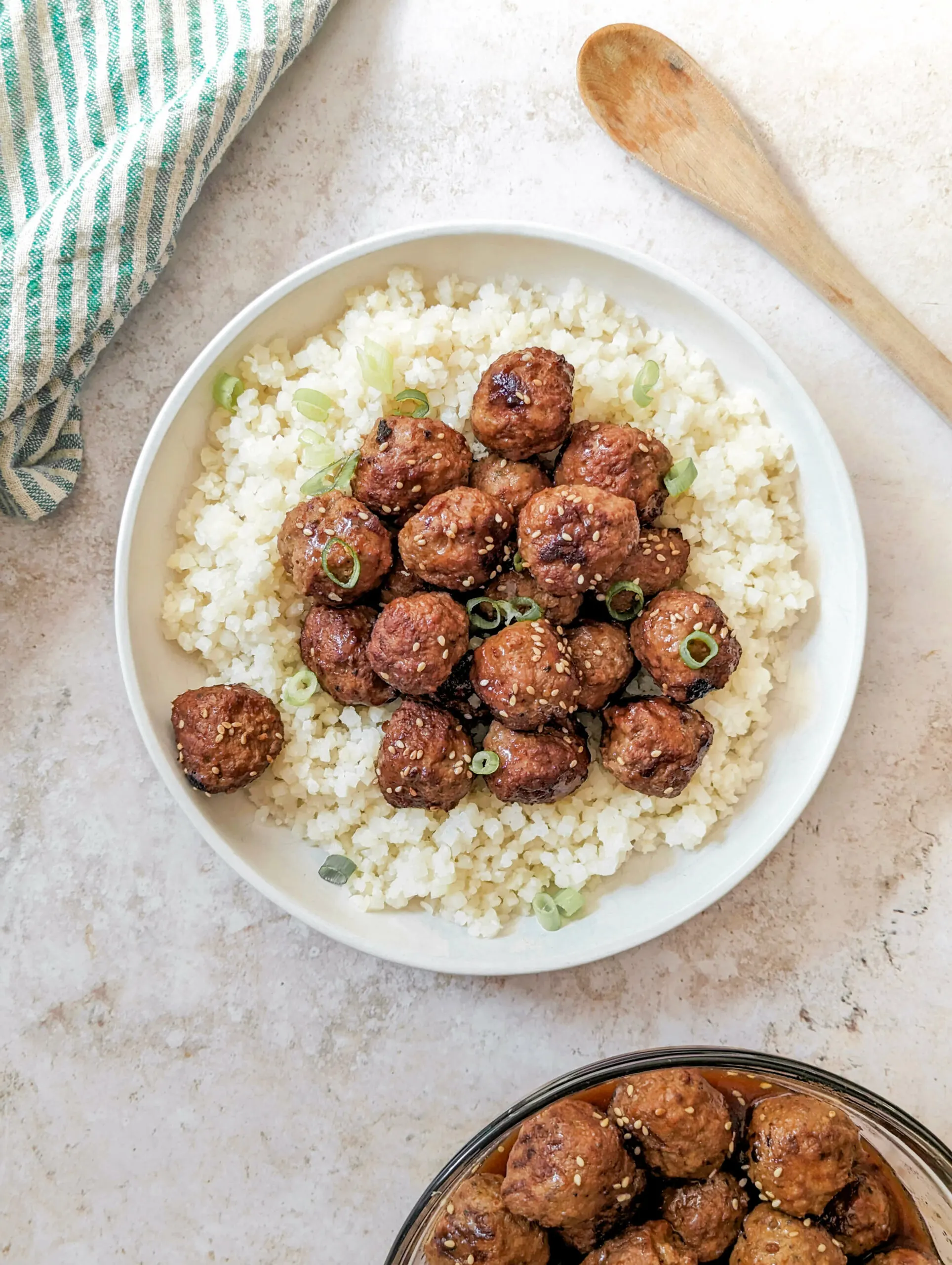 Instant Pot Frozen Meatballs served over cauliflower rice topped with scallions and a bowl of meatballs in the background.
