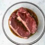 Steaks in a large bowl coated in a beer marinade.