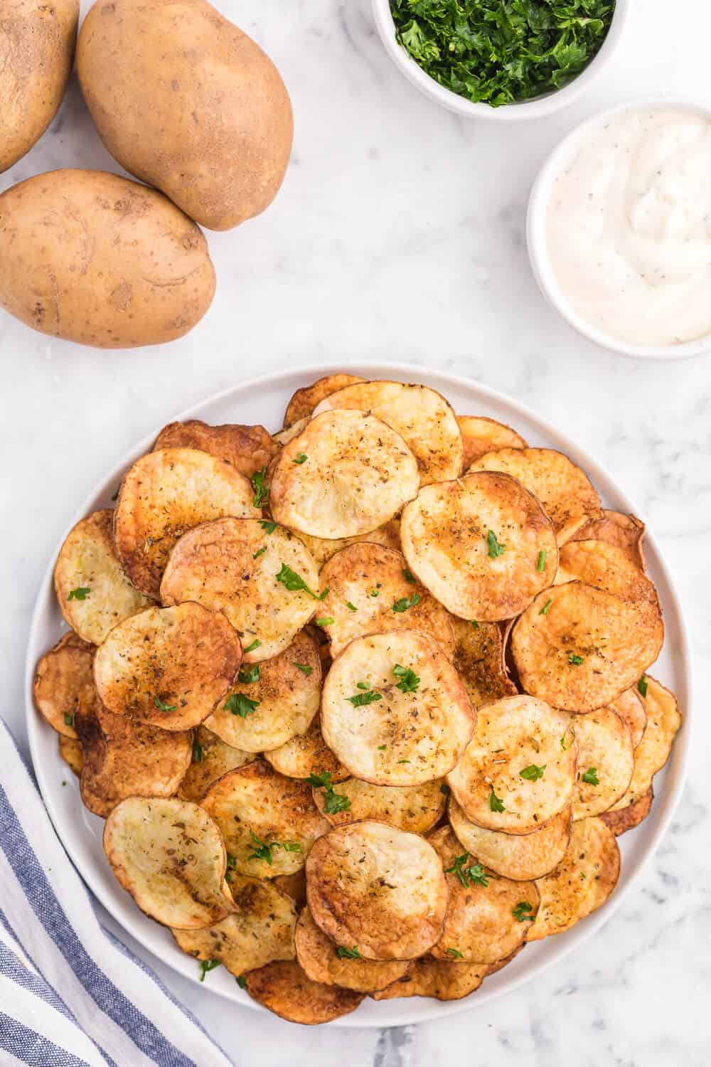 A plate of air fryer potato chips with russet potatoes in the background.