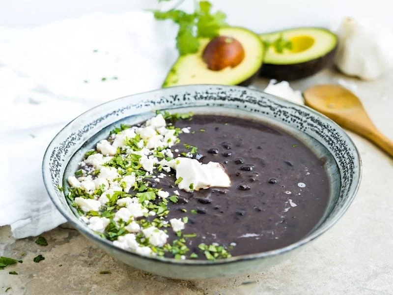 A bowl of black bean soup topped with cheese and cilantro. 