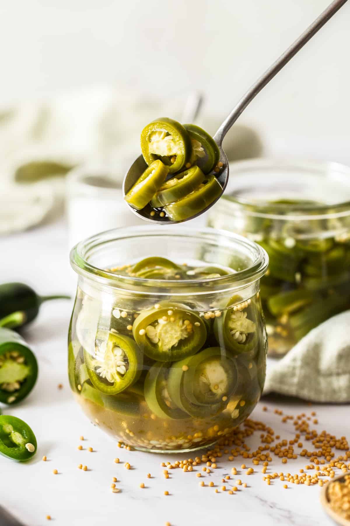 A spoon scooping pickled jalapeños out of a jar. 