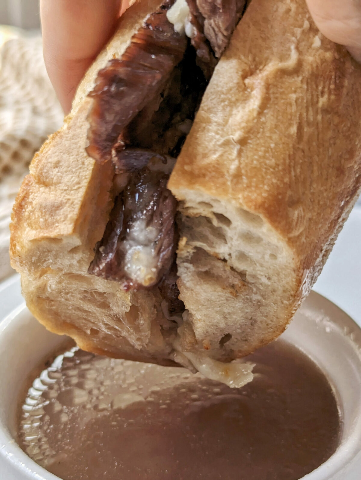 Air fryer french dip being dipped into au jus.