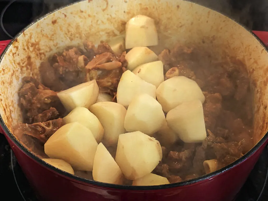 Potatoes added to the dutch oven full of simmering stew.