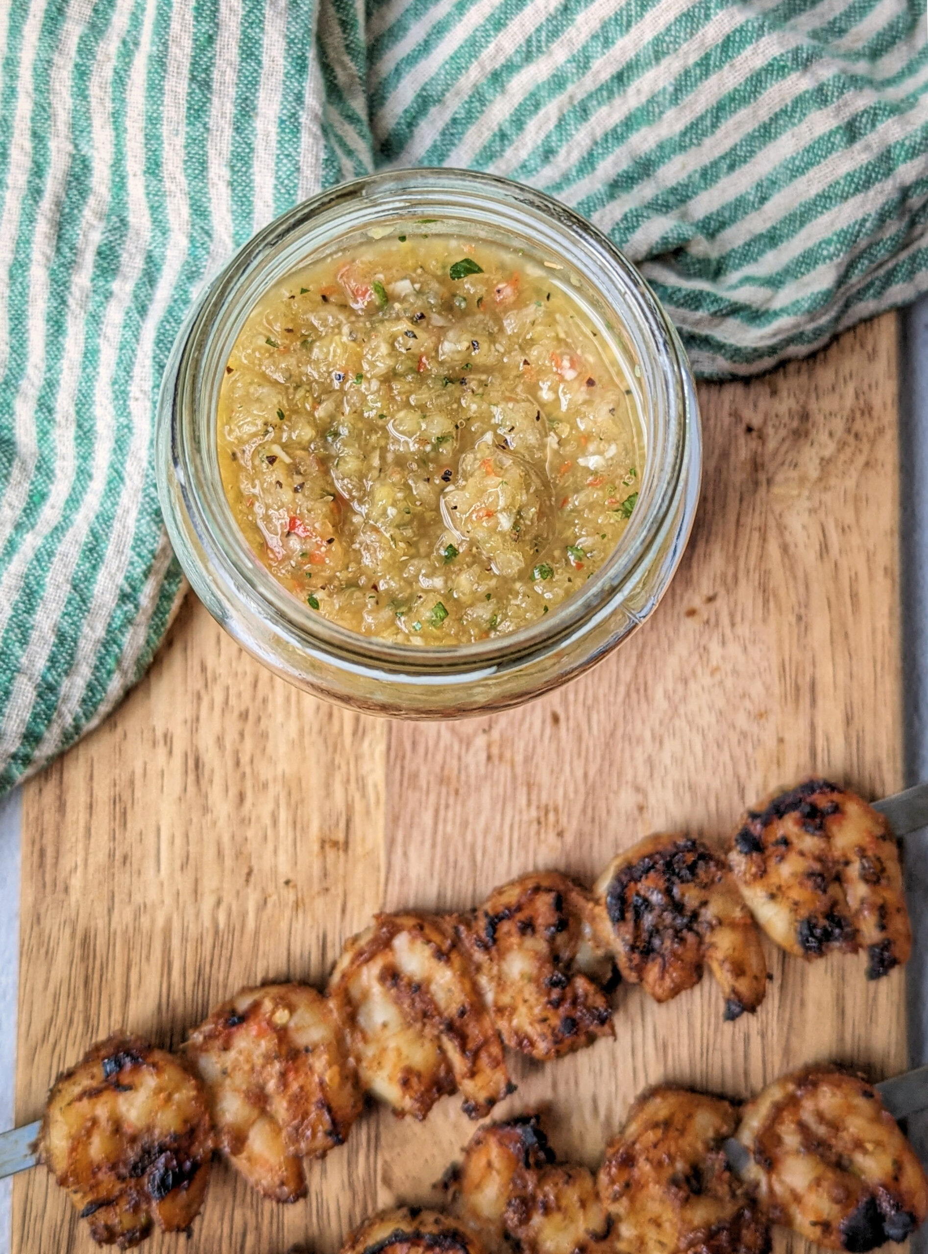 Caribbean Hot Sauce in a glass jar with shrimp skewers in the background.