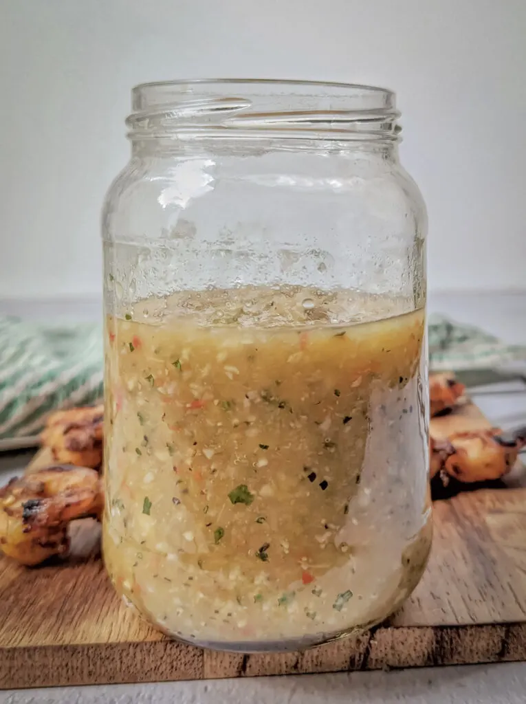 Caribbean Hot Sauce in a glass jar with shrimp skewers in the background.