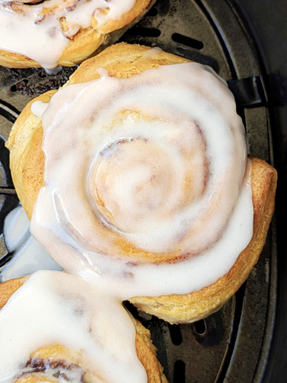 Cinnamon rolls in the air fryer with frosting on them.