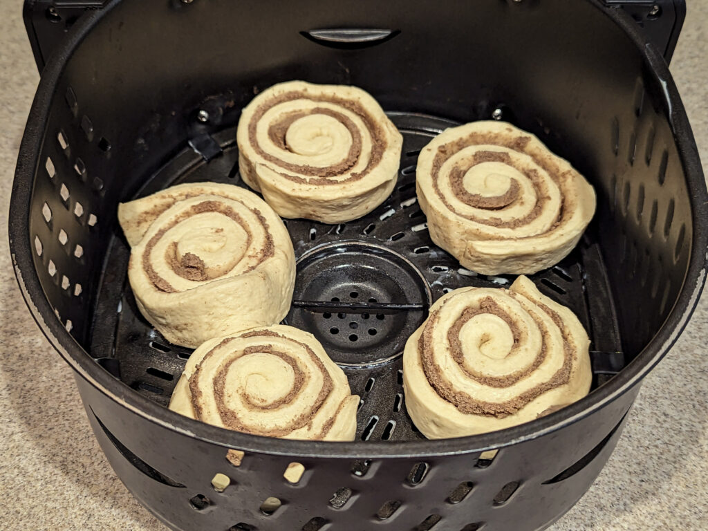 Uncooked cinnamon rolls lined into the air fryer basket.