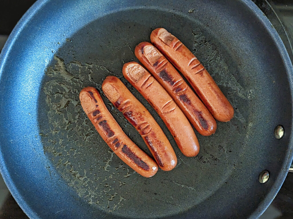 Hotdogs searing in a skillet.