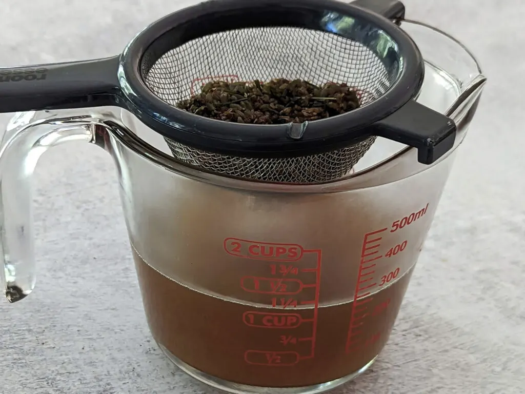Straining the lavender simple syrup into a container to remove the lavender buds.