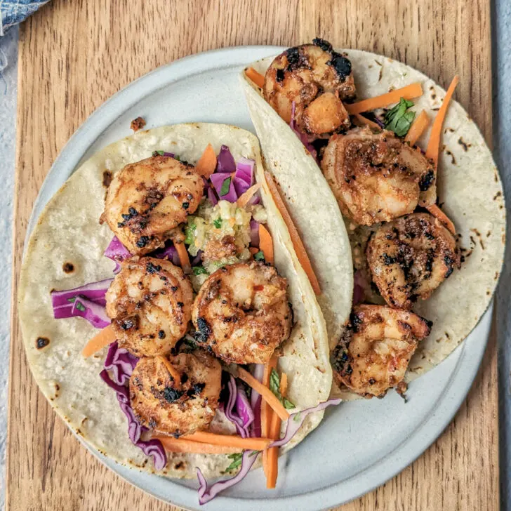 Jerk Shrimp Tacos on a plate garnished with slaw and Caribbean hot sauce.