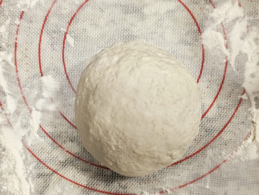 A smooth dough ball on a floured silicone mat.