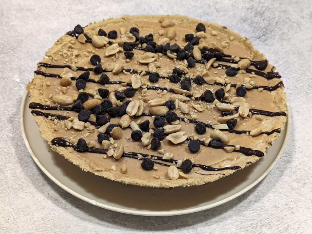 Our Silky Peanut Butter Pie garnished with melted peanut butter, chocolate sauce, chocolate chips, and peanuts.