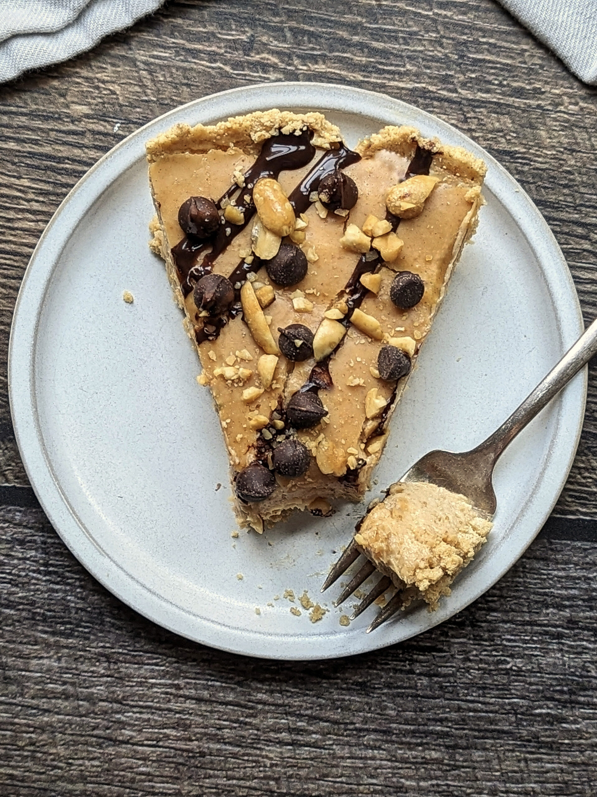 A slice of our Silky Peanut Butter Pie Recipe topped with chocolate syrup, melted peanut butter, chocolate chips, and peanuts.
