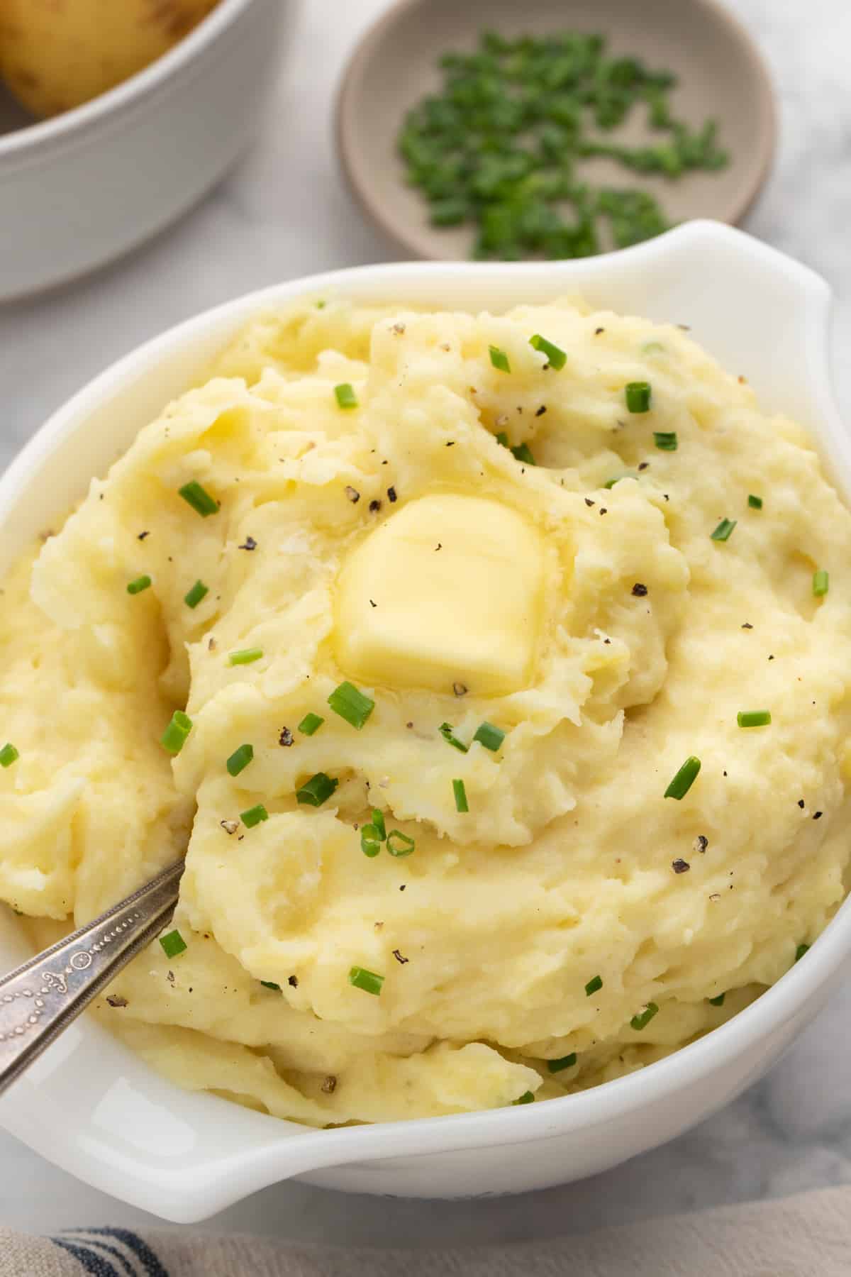 A bowl of mashed potatoes topped with butter and chives.