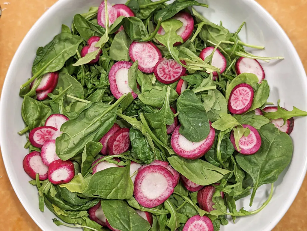 Arugula, spinach and cut up radishes in a serving bowl.