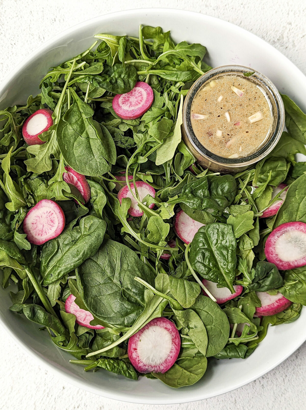 Arugula and Spinach Salad in a serving bowl with sherry shallot dressing.