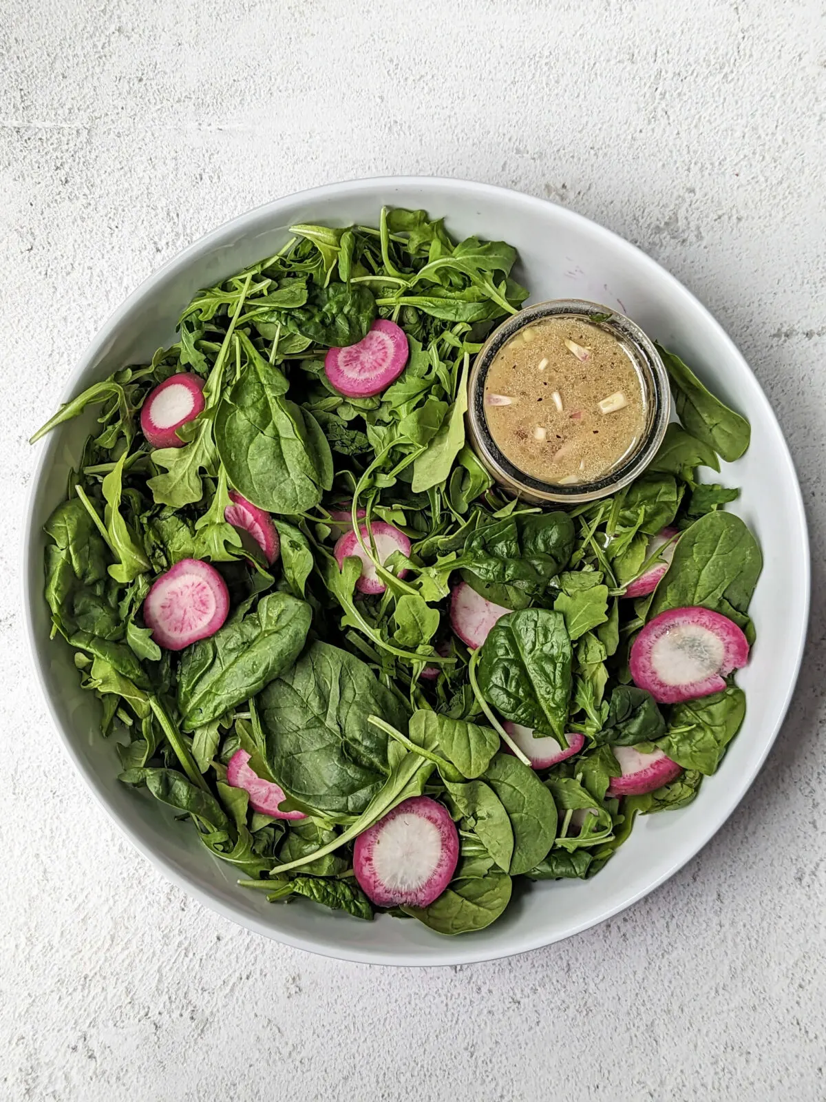 Arugula and Spinach Salad in a serving bowl with sherry shallot dressing.