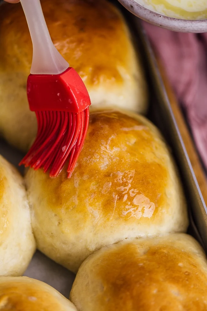 A pastry brush brushing butter onto homemade yeast rolls. 