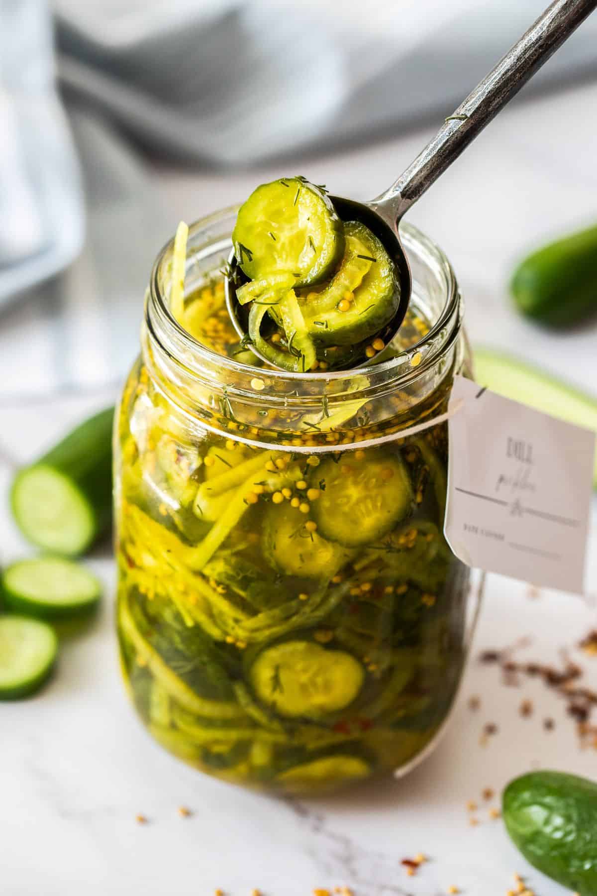 A jar of sliced dill pickles with a spoon scooping some of it out. 